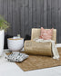 Pico outdoor cushion with deep olive tribal lines on white background placed on a brown outdoor rug with the Ano cushion on a rattan chair with a throw