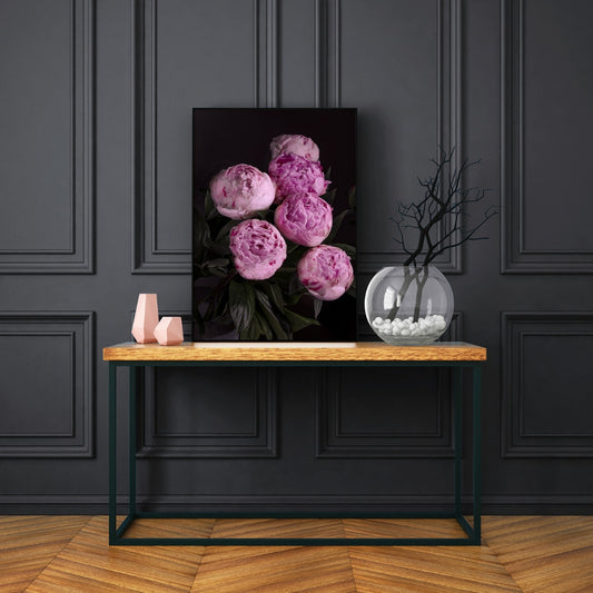 bunch of pink peonies on a black back ground sitting on a wooden table withi black legs against a dark blue paneled wall and wooden parquet flooring