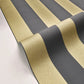 A close-up of a rolled sheet of wallpaper or fabric featuring alternating metallic gold and dark charcoal gray stripes, displayed on a clean white surface.