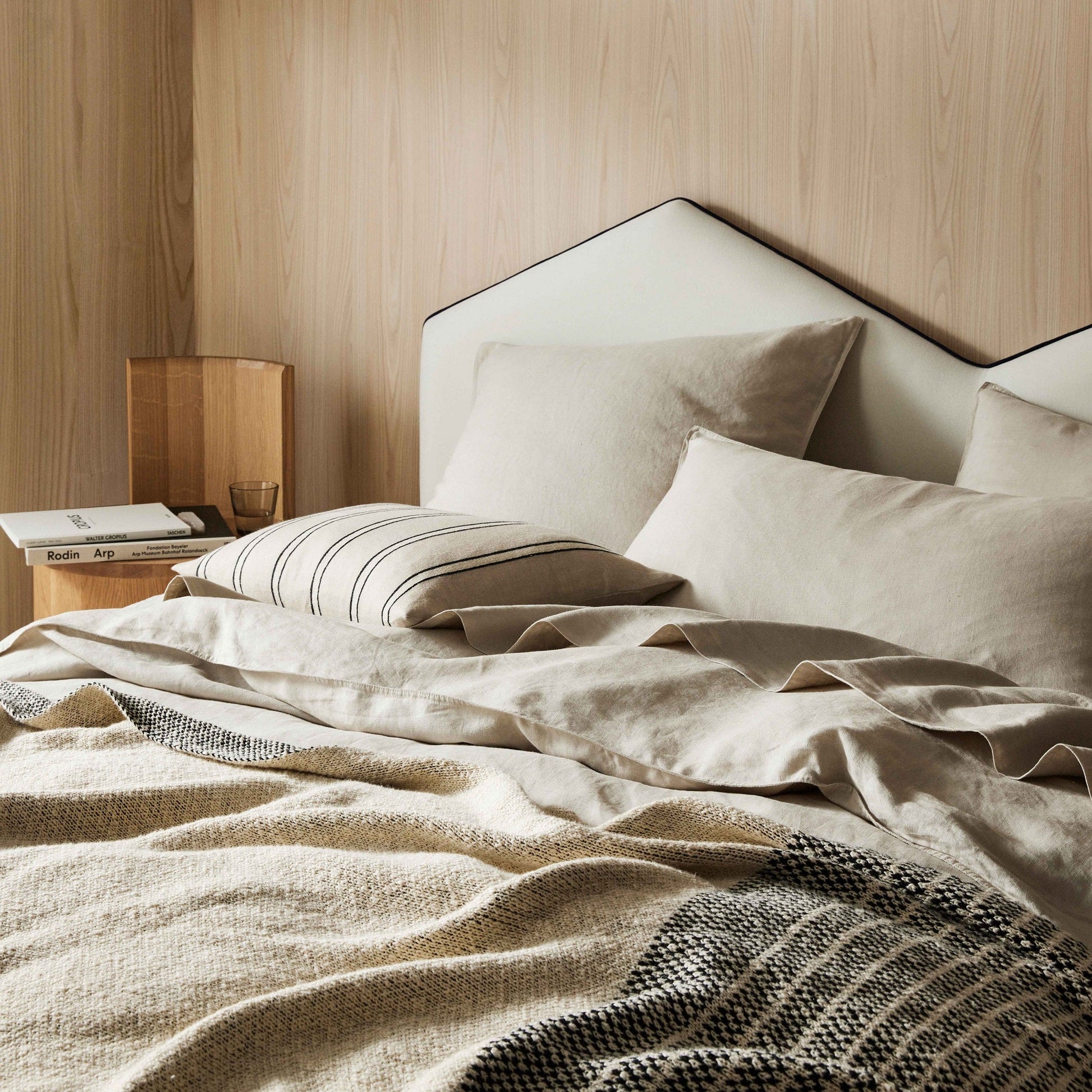 Neatly made bed with beige bedding against a wooden wall.