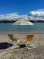 Two beach chairs under a striped umbrella on a sandy beach with ocean and sky in the background.