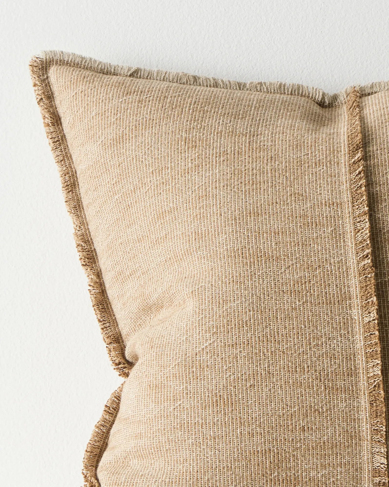 Beige pillow with textured fabric and frayed edges on a light background