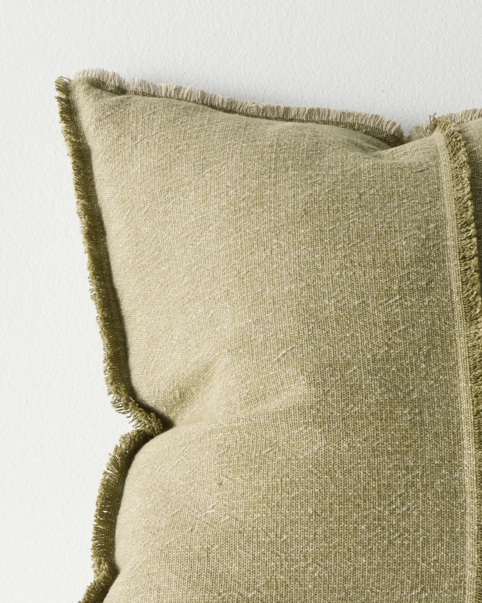 Textured green pillow with frayed edges on a light background