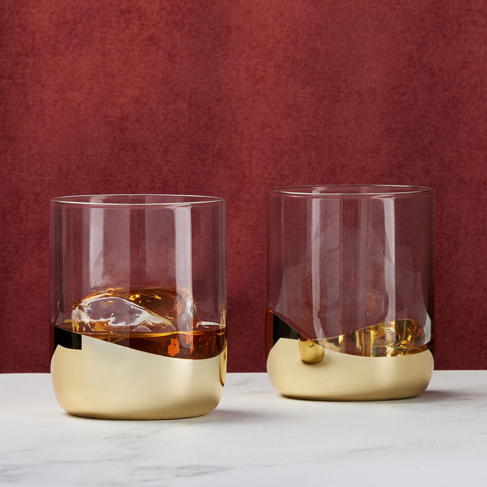 Two glasses with gold bases and clear bodies on a white surface with a red background