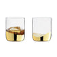 Two clear glasses with gold liquid and ice cubes on a white background