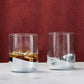 Two glass tumblers with metallic bases on a white surface against a red background