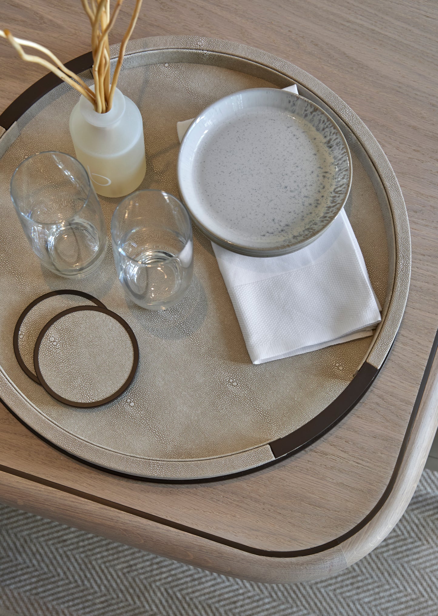 Round shagreen tray with ceramic plate, glasses, and coasters on a wooden surface.