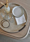 Round shagreen tray with ceramic plate, glasses, and coasters on a wooden surface.