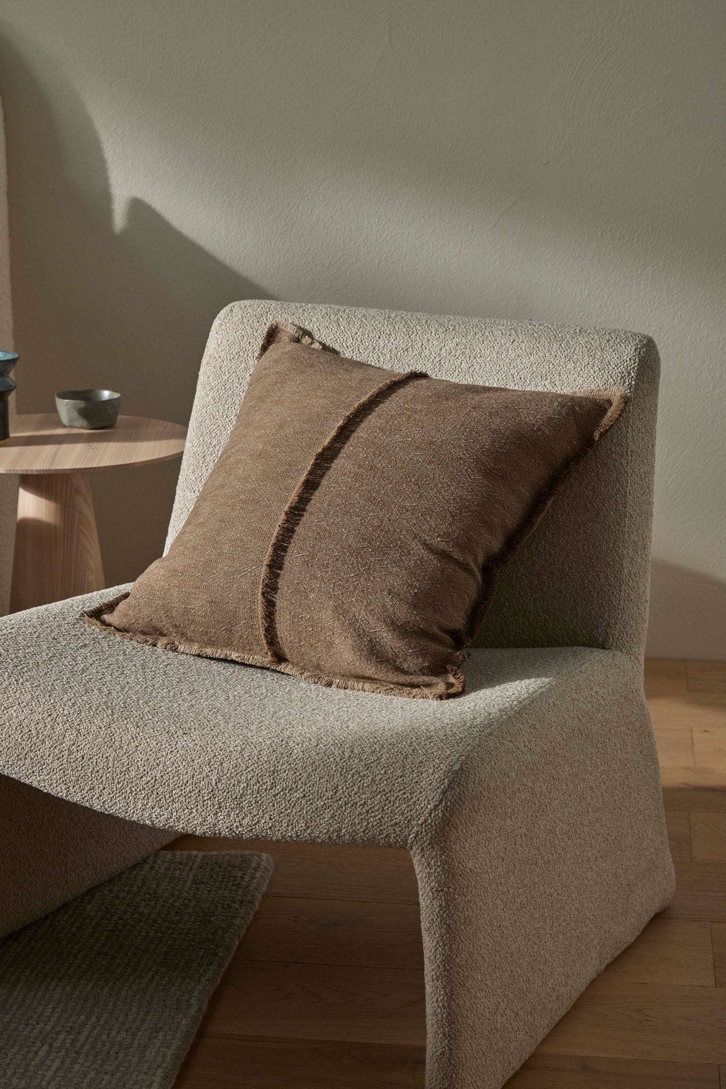 Beige armchair with a brown pillow in a minimalistic room.