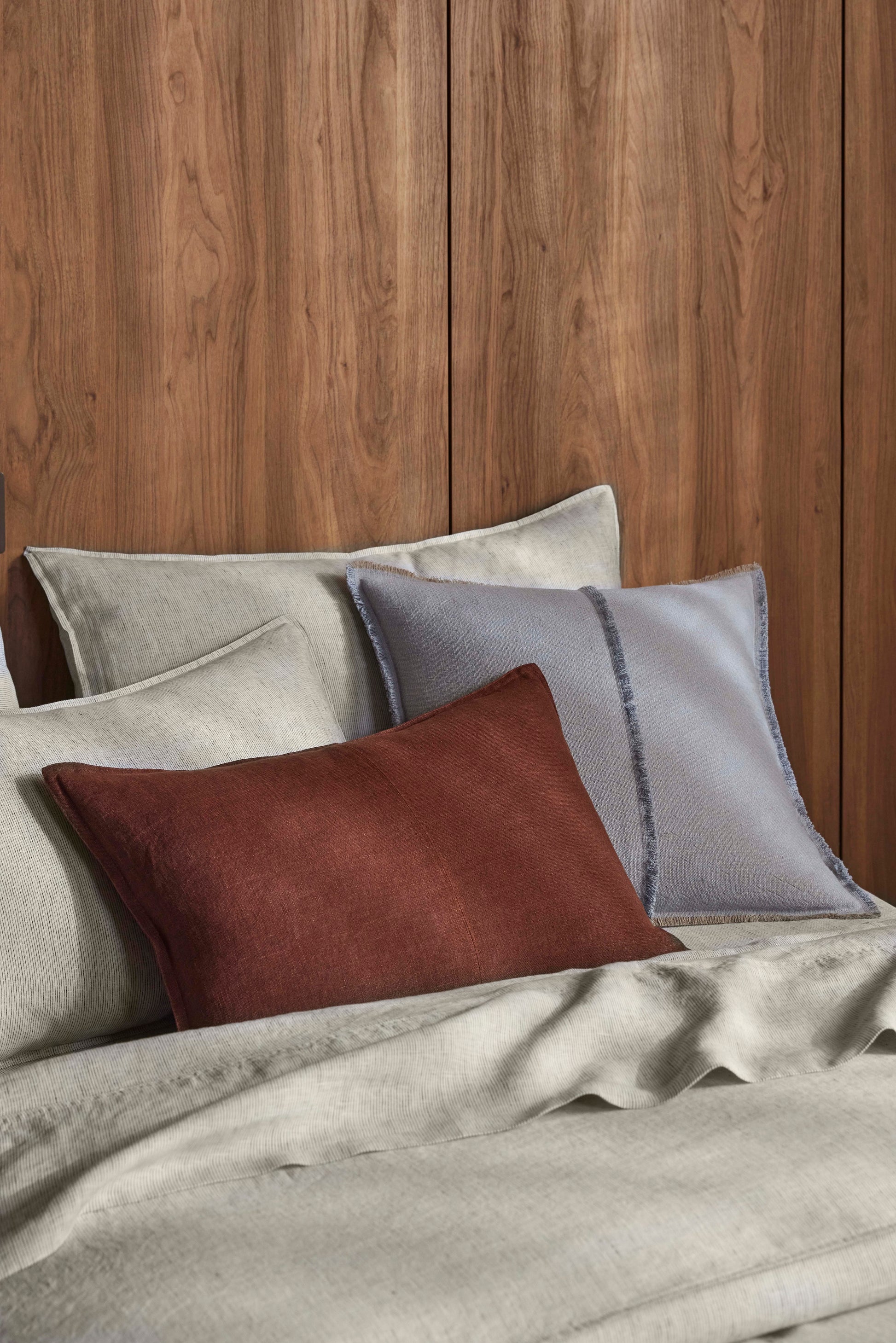 Gray bedding with a brown pillow against a wooden wall.