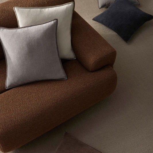 Brown sofa with various colored cushions on a neutral background