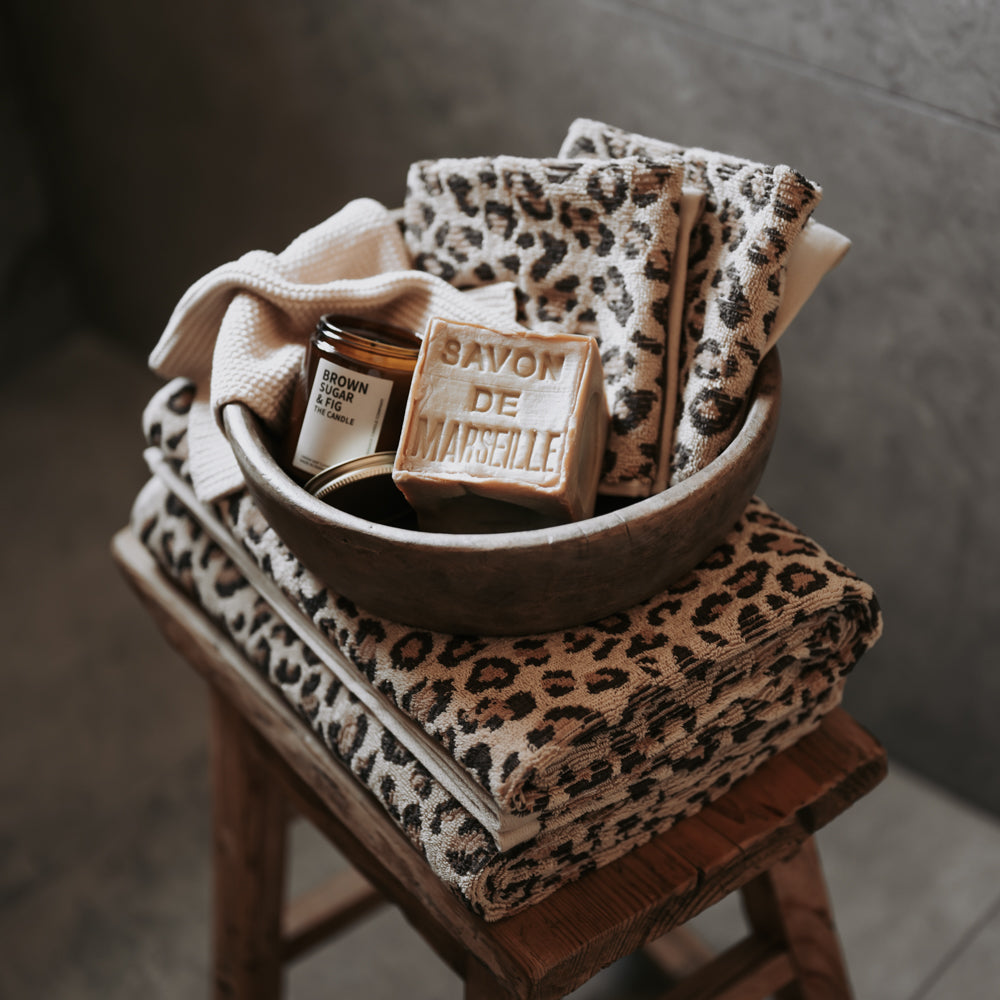 Leopard print towels and soap in a bowl on a wooden stool with a neutral background