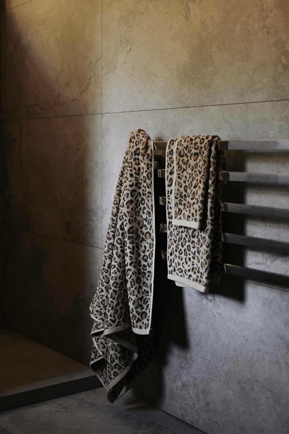 Leopard print towels hanging on a towel rack against a tiled wall.