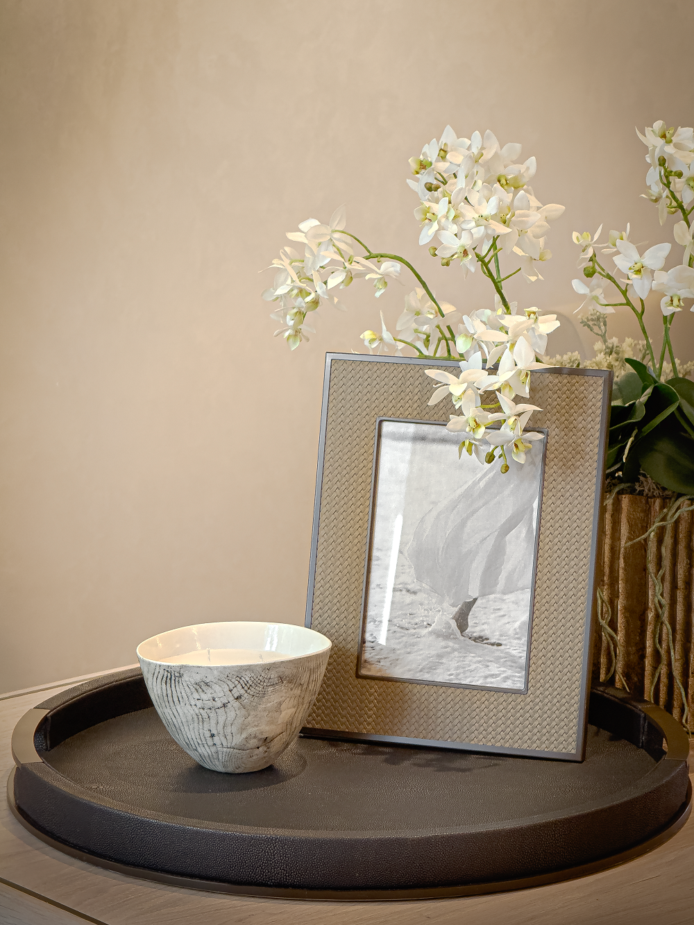Decorative setting with a bowl, photo frame, and flowers on a wooden surface.