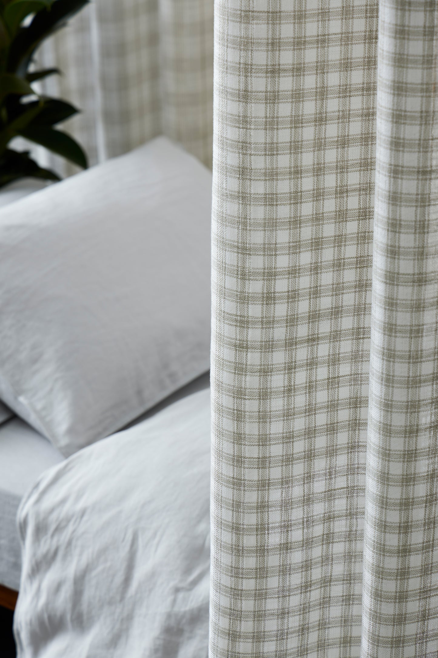 Plaid curtain partially covering a bed with white bedding