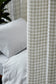 Plaid curtain partially covering a bed with white bedding
