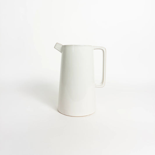 A minimalist white ceramic pitcher with a tapered body, a short spout, and a rectangular handle, photographed on a seamless white background.