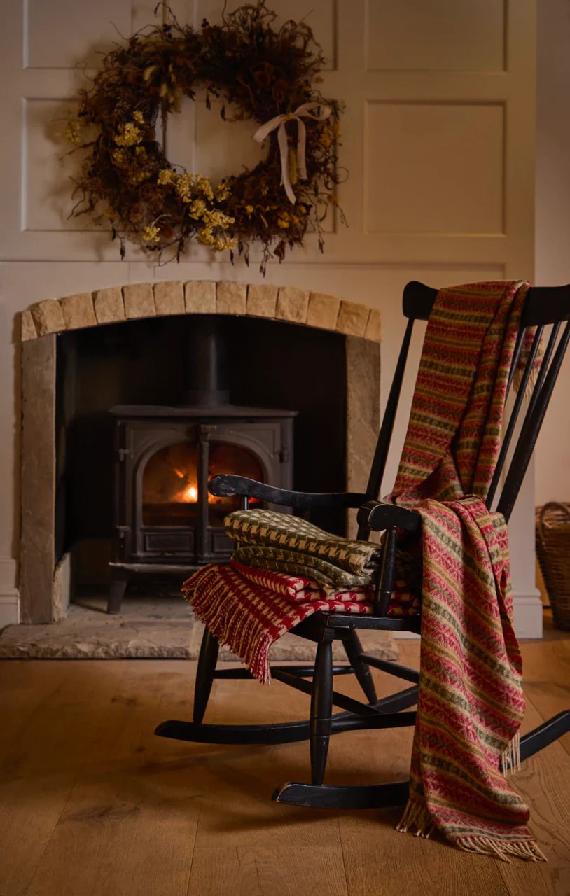 Cozy living room with a fireplace, chair draped with a blanket, and wreath on the wall.