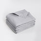 A folded light gray quilted comforter or duvet with a matching pillowcase, neatly stacked on a clean white studio background. Feather filled
