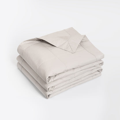 A neatly folded light beige comforter or duvet with matching pillowcases, stacked on a clean white background.