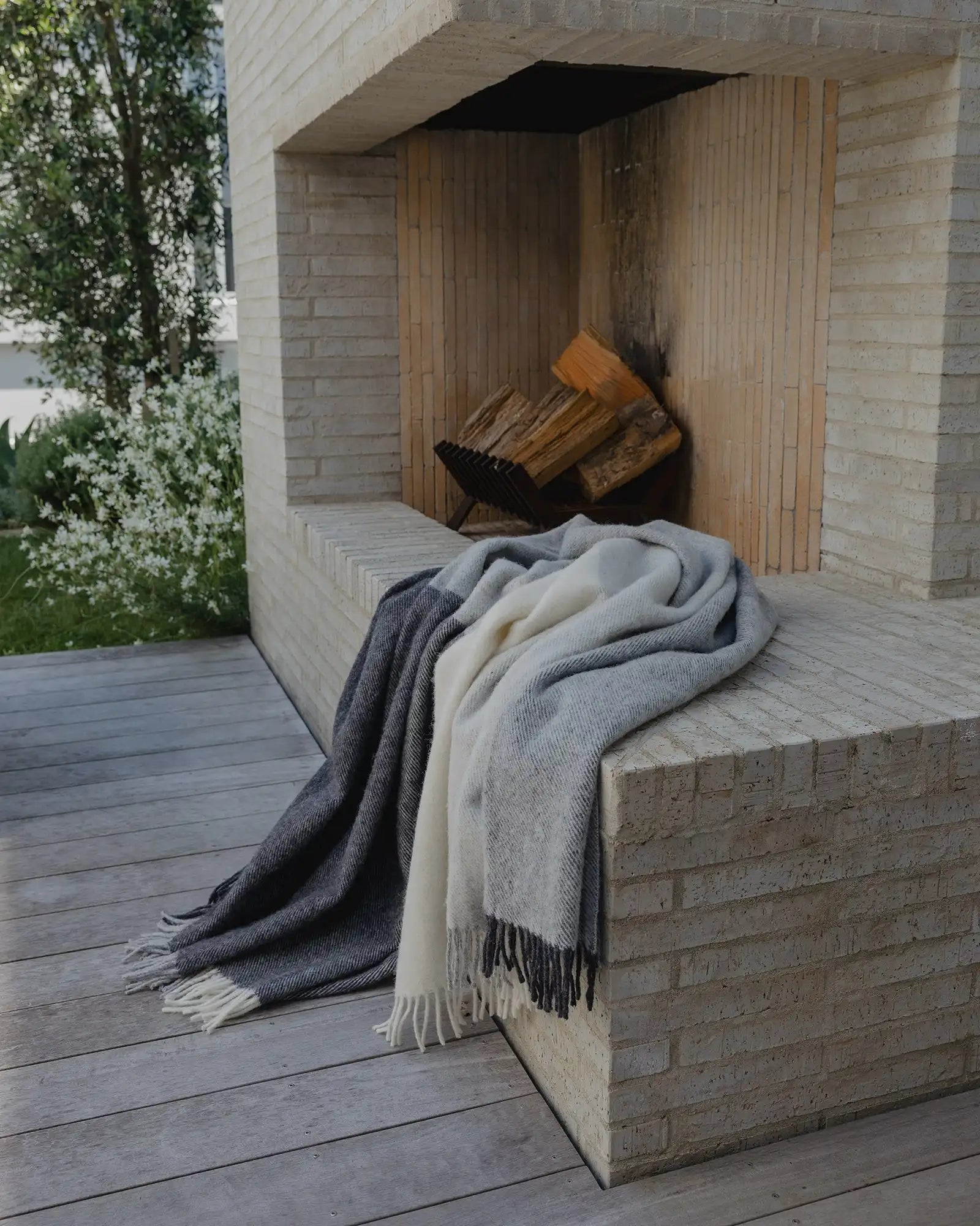 Three blankets draped over a stone bench next to a fireplace with firewood.
