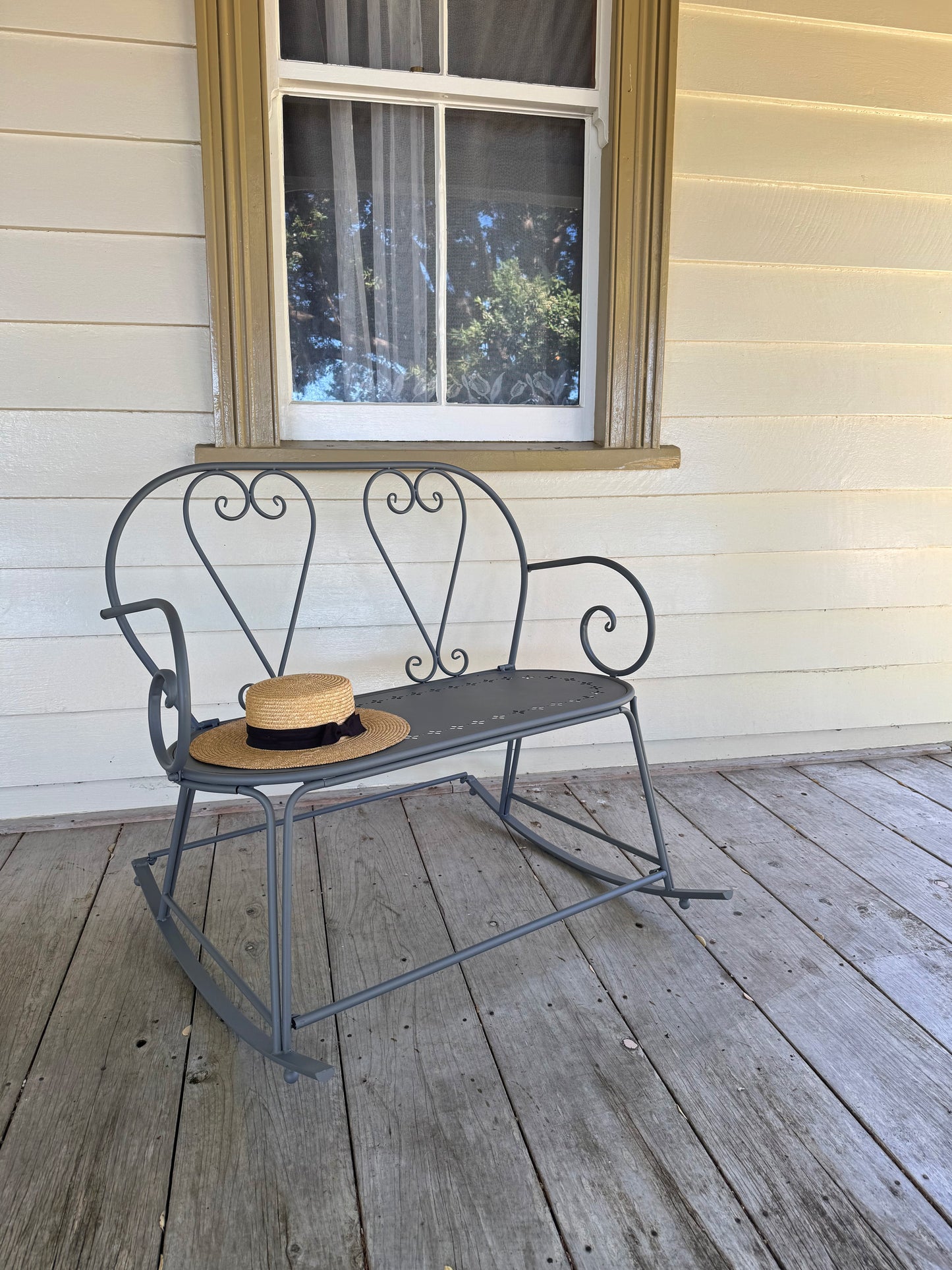 Metal rocking chair on a wooden porch with a window in the background