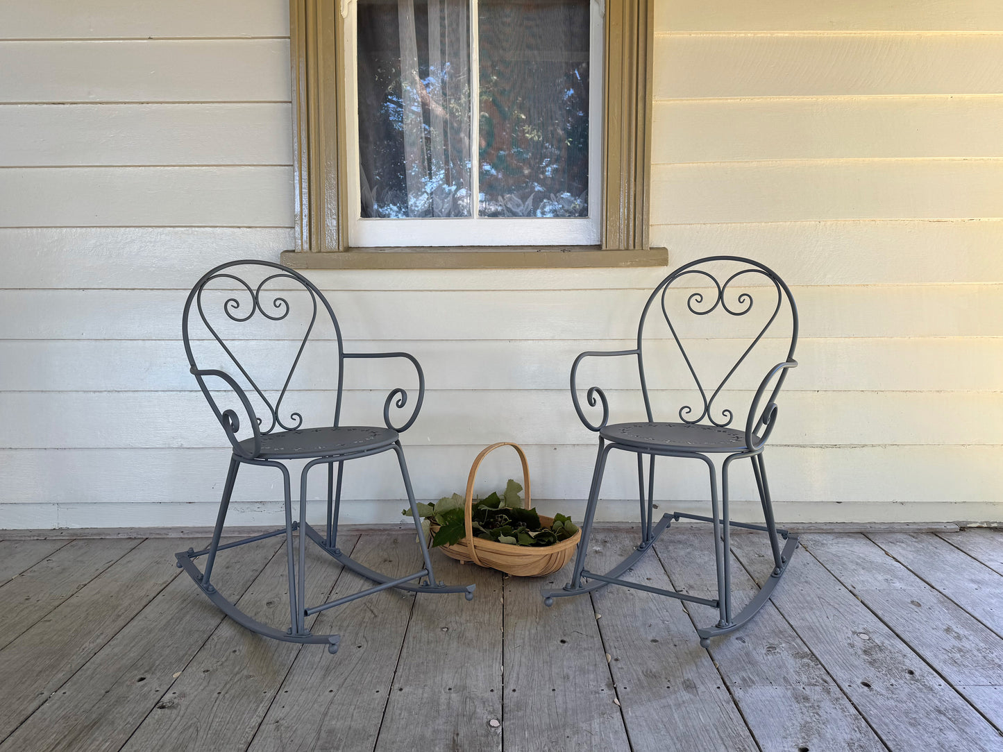 Two metal rocking chairs on a wooden deck with a window in the background.