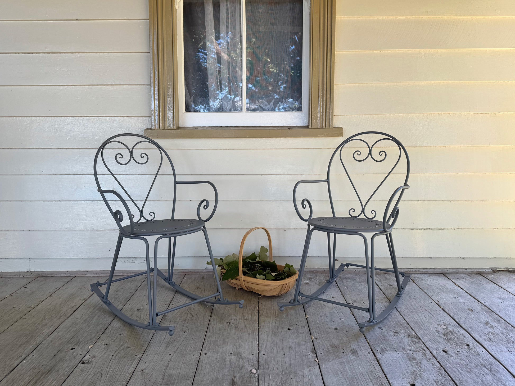 Two metal rocking chairs on a wooden deck with a window in the background.
