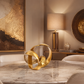 gold fluid sculpture on a cream marble dining room table with gold and bronze artwork, lamp and decor in the background