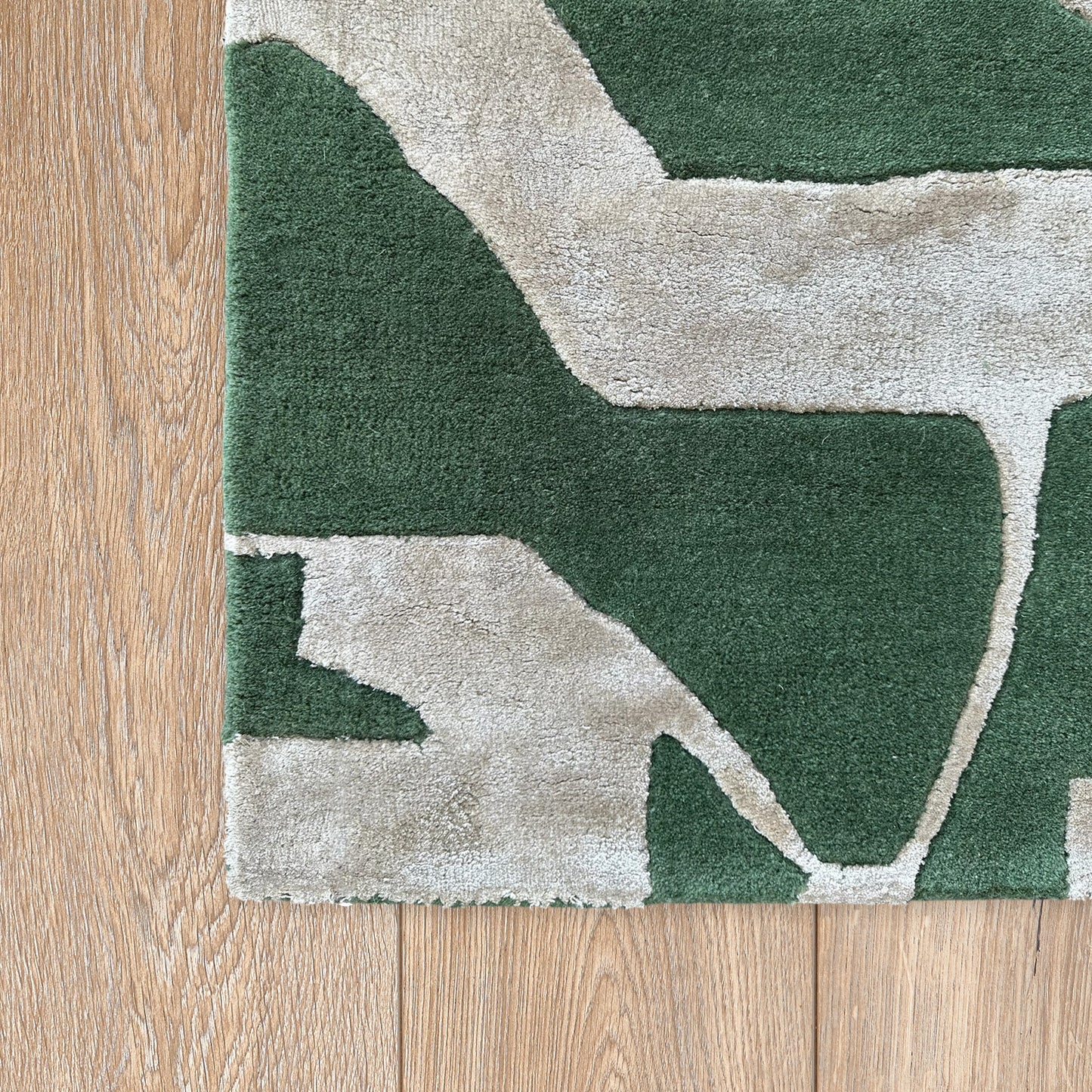 Green and beige abstract patterned rug on a wooden floor