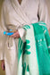 Person wearing a white robe holding a green towel with white patterns.