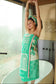Woman wrapped in a green towel with a pattern, standing in a bathroom.