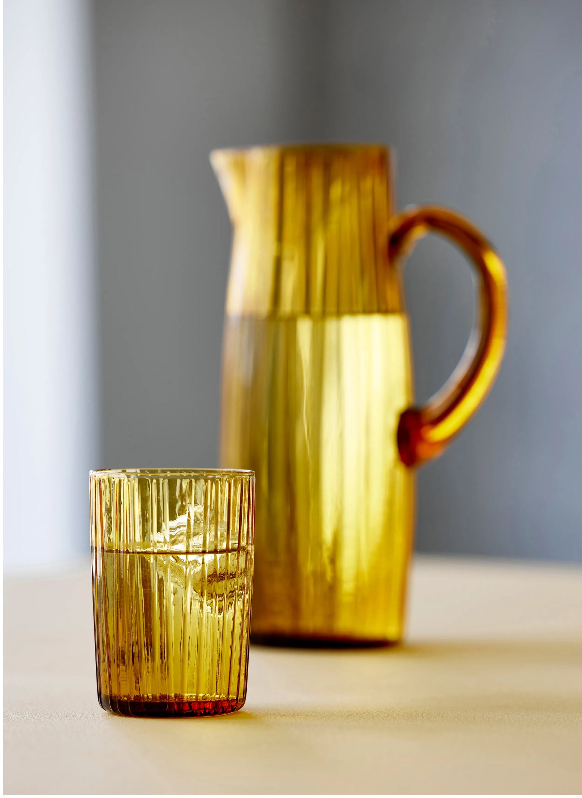 Amber-colored pitcher and glass on a neutral background