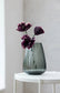 Glass vase with purple flowers on a white table against a light gray wall