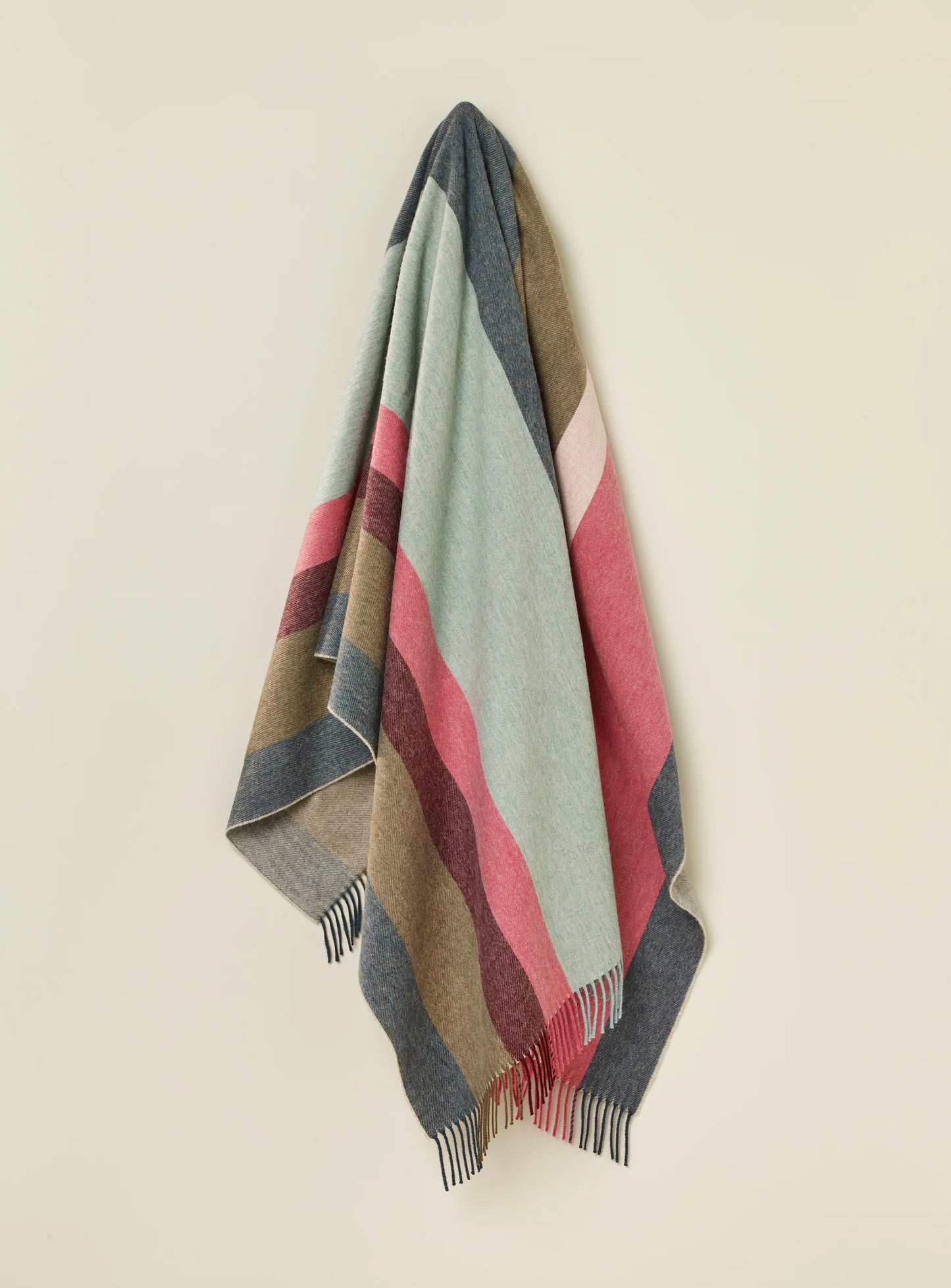 Striped blanket with red, green, and brown colors draped over a light beige background