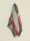 Striped blanket with red, green, and brown colors draped over a light beige background
