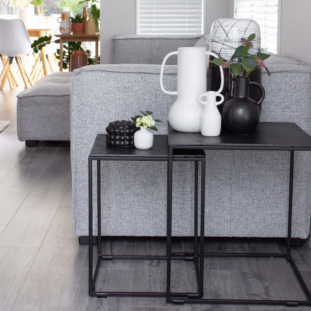 Modern living room with gray sofa, black side tables, and decorative vases.