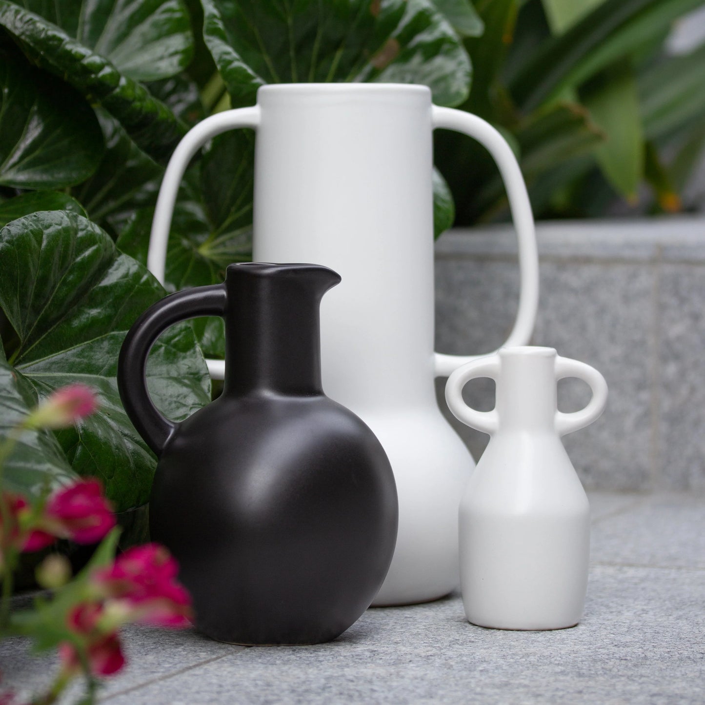Group of black and white vases and jug with handles with foliage around