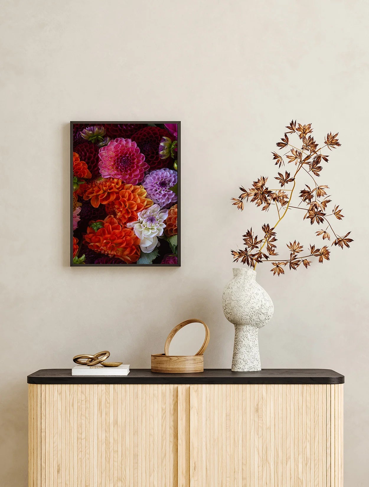 Decorative setup with a floral painting, vase, and branch on a shelf against a beige wall.