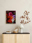 Decorative setup with a floral painting, vase, and branch on a shelf against a beige wall.