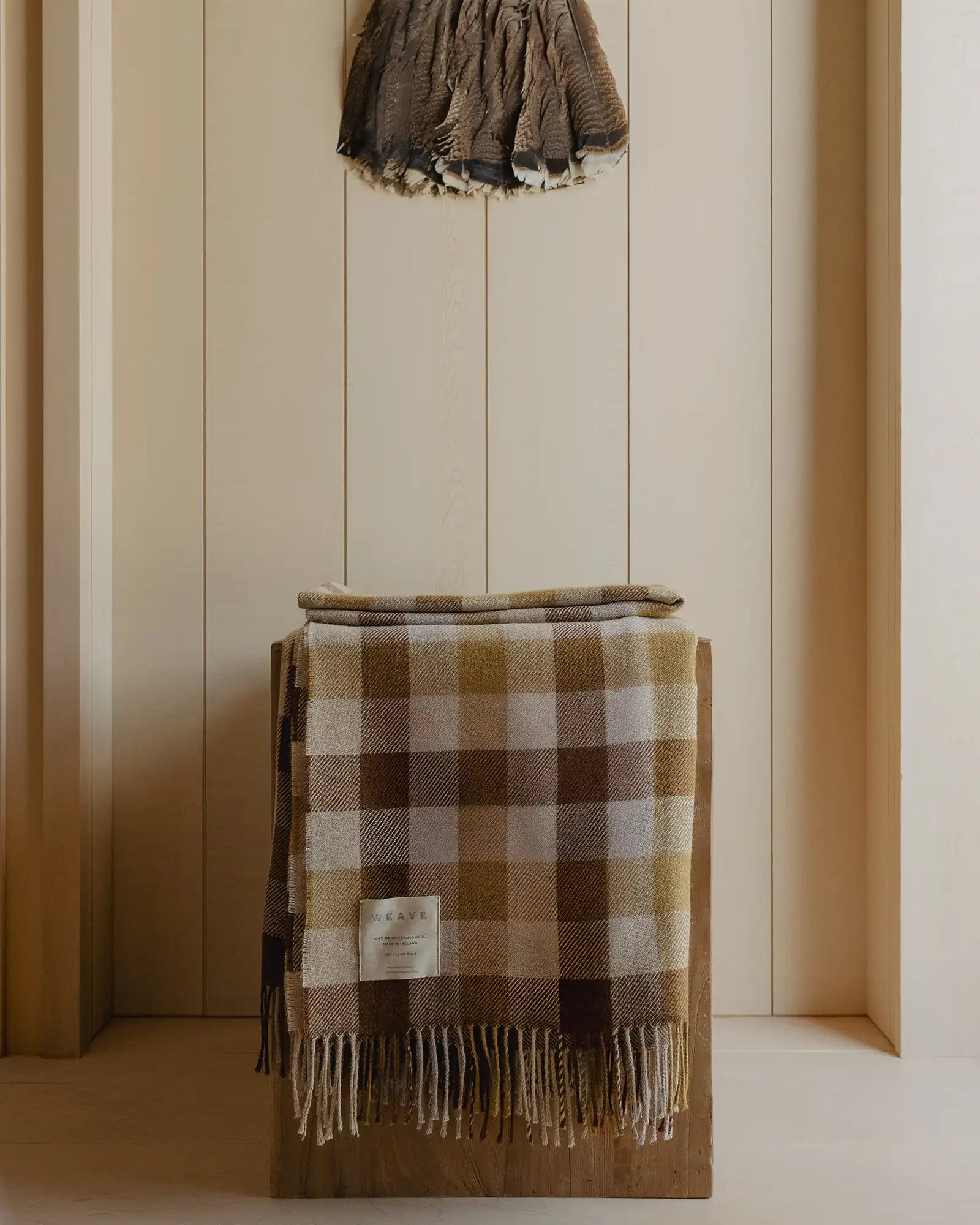 Plaid blanket draped over a wooden box against a striped wall.