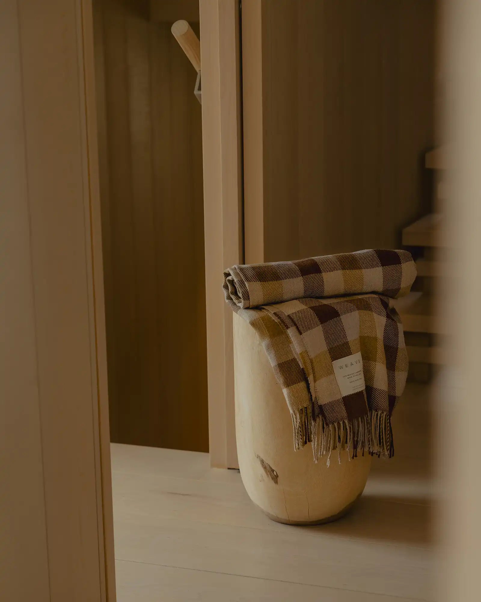 Plaid blanket draped over a wooden stool against a neutral wall.