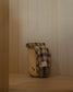 Plaid blanket draped over a wooden barrel against a wooden paneled wall.