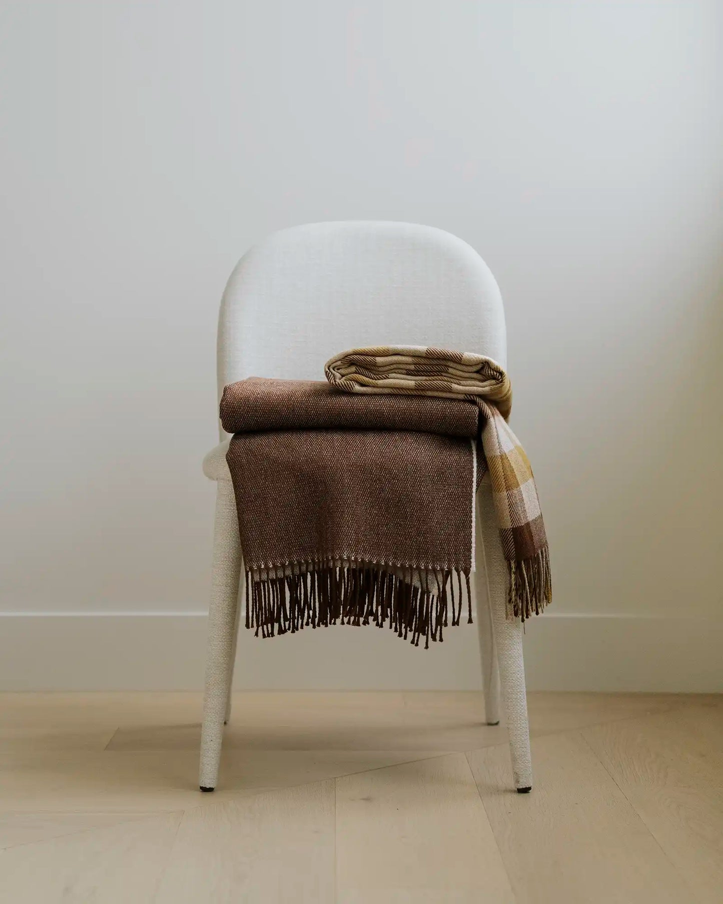 Brown plaid blanket draped over a white chair against a plain wall.