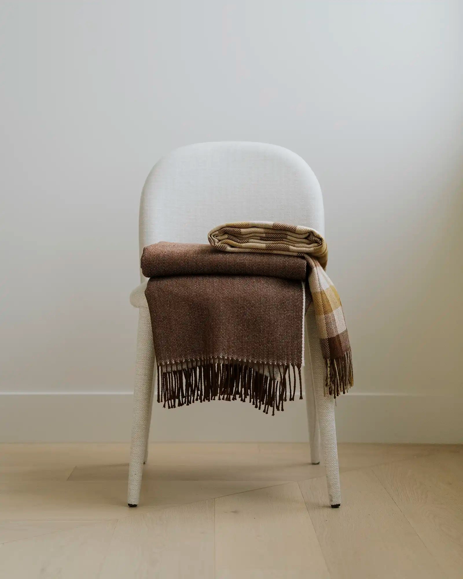 Brown plaid blanket draped over a white chair against a plain wall.