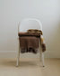Brown plaid blanket draped over a white chair against a plain wall.