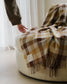 Plaid blanket draped over a chair with a blurred hand reaching towards it, set against a neutral background.
