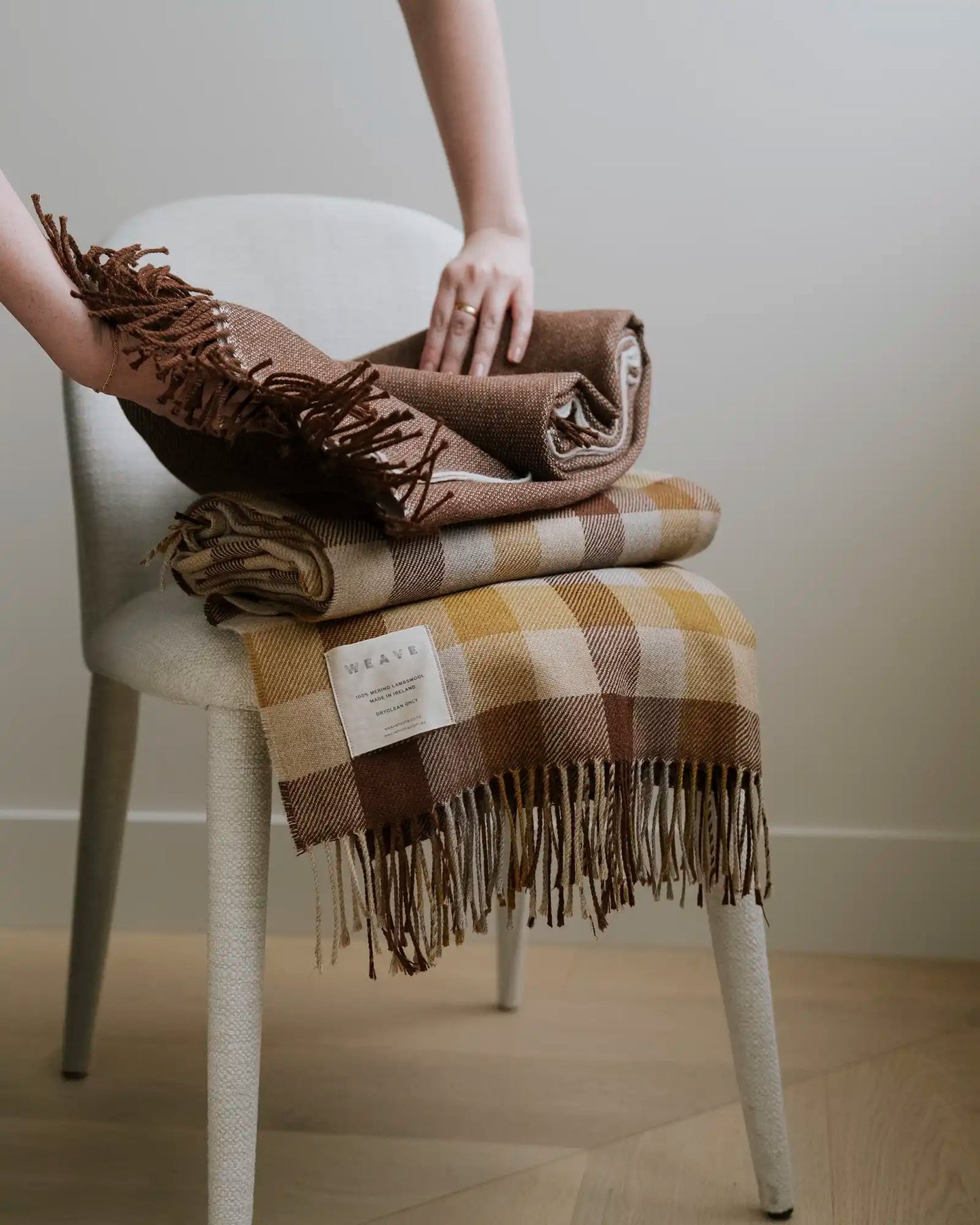 Person holding a folded brown plaid blanket on a white chair.