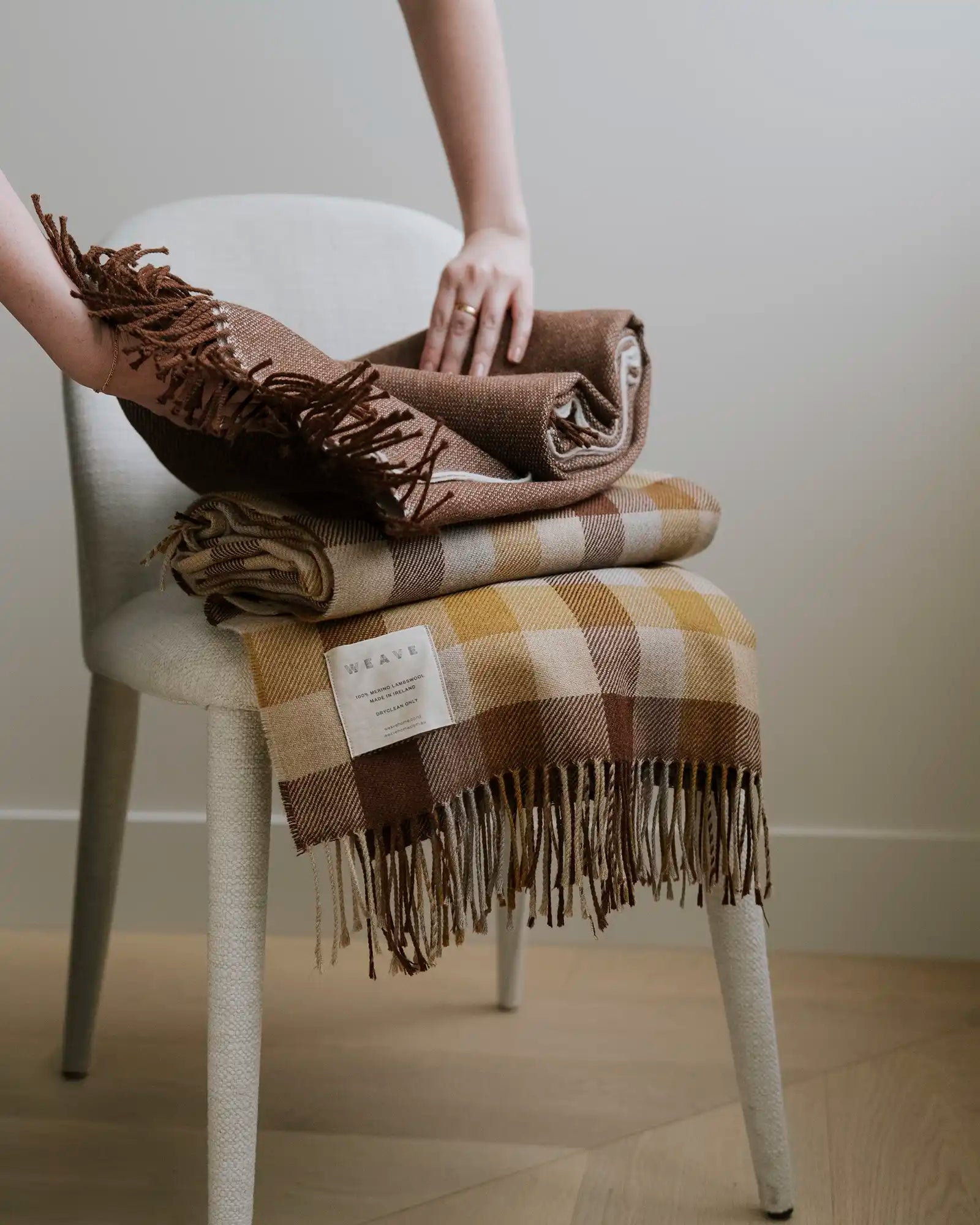 Person holding a folded brown plaid blanket on a white chair.