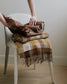 Person holding a folded brown plaid blanket on a white chair.